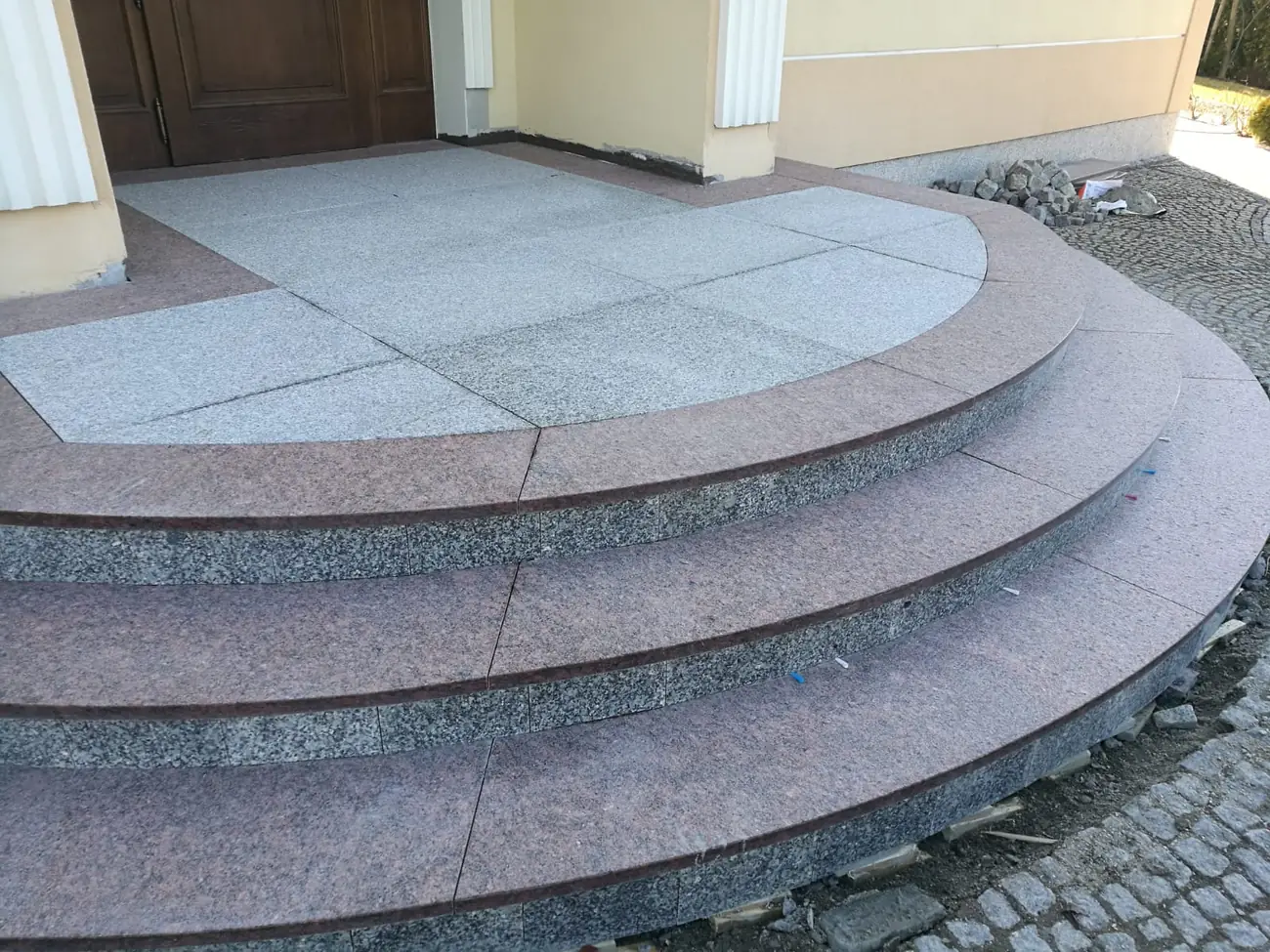 Półokrągłe dwukolorowe schody granitowe przed wejściem do domu
